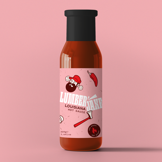 A single bottle of 'Lumberjaxe Louisiana Hot Sauce' displayed against a solid pink background. The bottle has a black cap and a pink label featuring a bearded lumberjack character wearing a red hat, looking flustered with steam coming from his head. The design includes an illustration of a red chili pepper and an axe. The label highlights the sauce’s spiciness with a 'Hot Stuff!' badge and indicates a weight of 220g (7.4 fl oz).